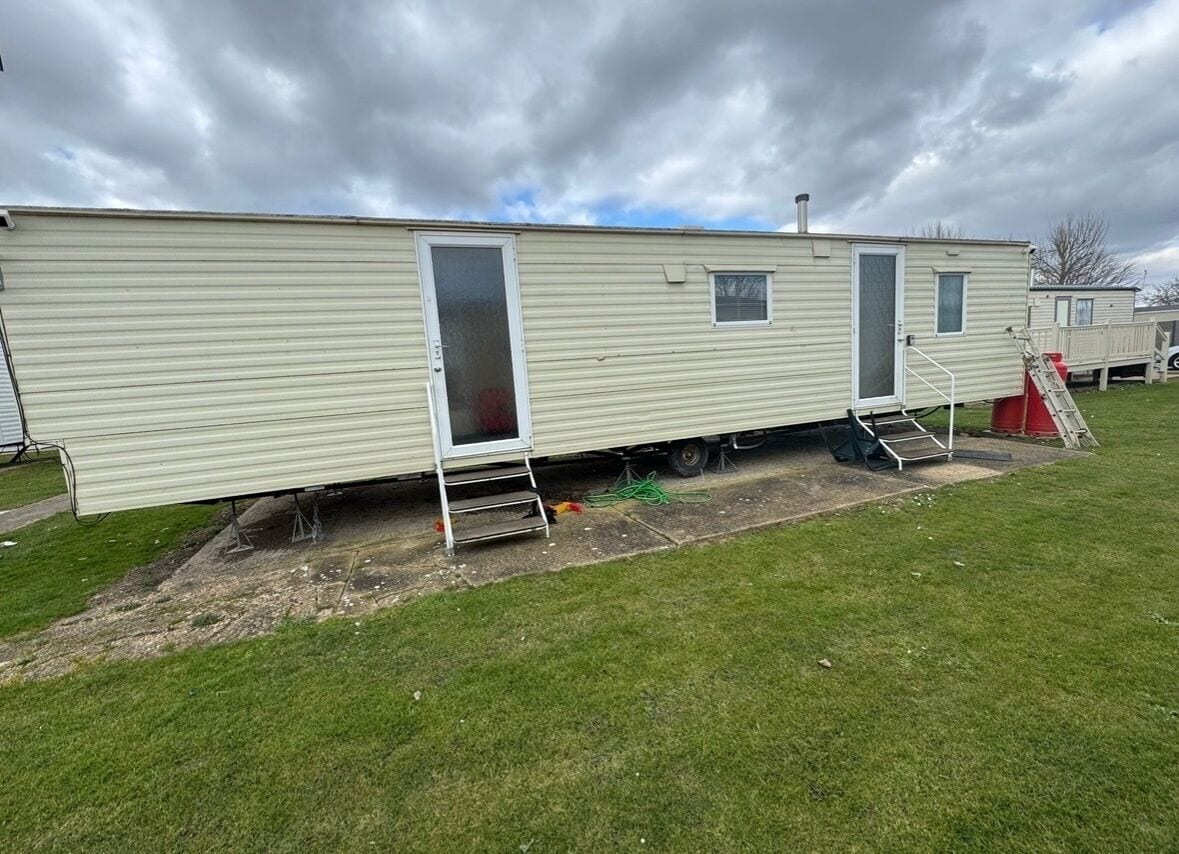 A mobile home with a sliding door, a small window, and a ramp leading to the door.