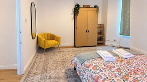 Ein Schlafzimmer mit einem Bett, einem gelben Sessel, einem Kleiderschrank und einem Spiegel.