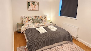 Ein Schlafzimmer mit Bett, Kissen, einem Nachttisch, einer Heizung und einem Fenster mit Jalousie.