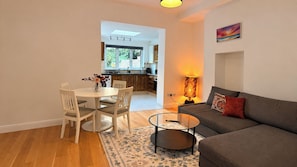 Ein modernes Wohnzimmer mit einem grauen Sofa, einem runden Couchtisch und einem Essbereich mit einem weißen Tisch und Stühlen.