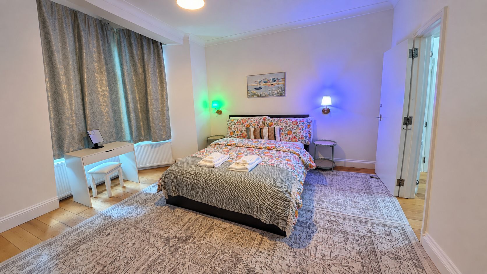 Een slaapkamer met een bed, nachtkastje, stoel, lamp en een schilderij aan de muur.