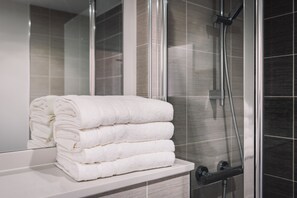 A bathroom with a glass shower enclosure, a white sink, and a stack of white towels. - Birmingham City Apartment! - Fast WiFi & Sleeps 5 (Birmingham)