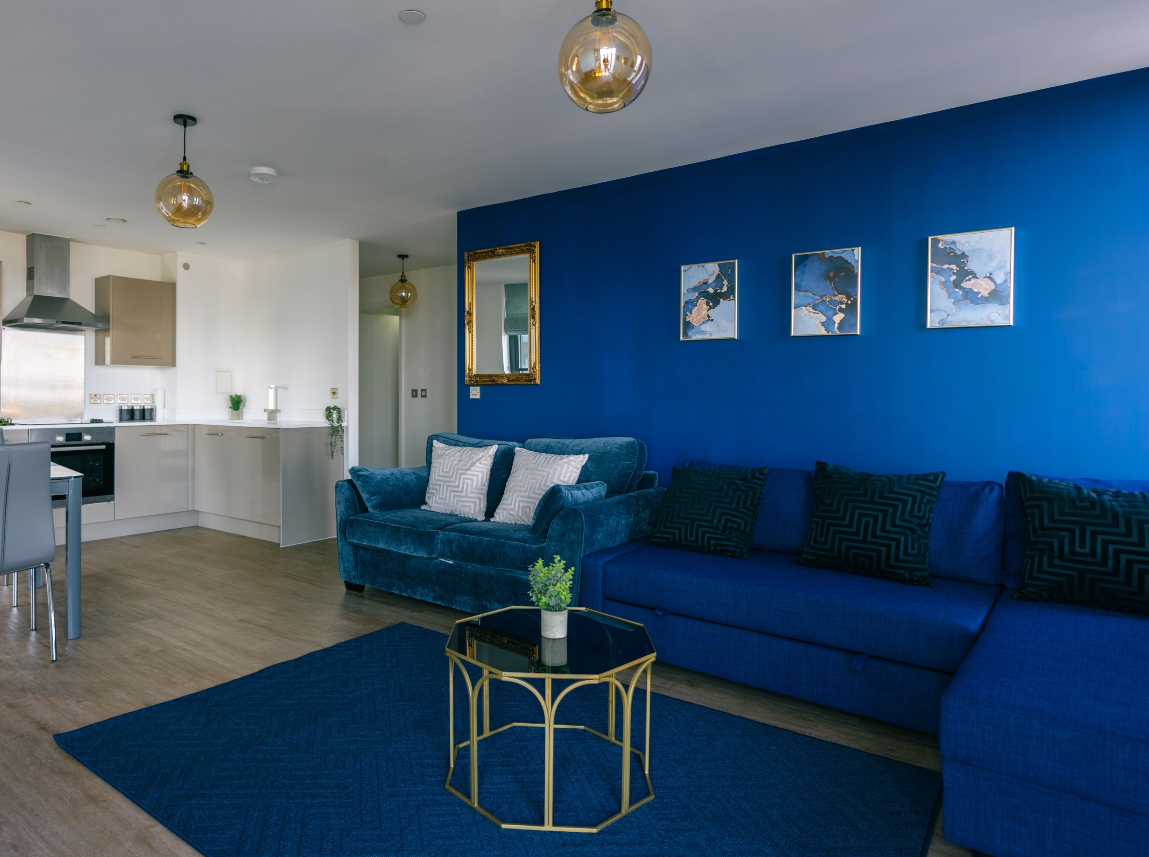 Una sala moderna con un sofá azul, una mesita de centro y una cocina al fondo.