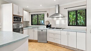 A modern kitchen with white cabinetry, a stainless steel range hood, a built-in microwave, and a dishwasher. - Nelson On The Hill close to Nelson City (Nelson)