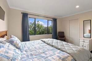 Ein Schlafzimmer mit zwei Betten, einem Sessel, einer Kommode und einem großen Fenster mit Vorhängen.