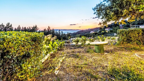 Un jardí amb una banca de pedra, diferents plantes i una vista a un paisatge llunyà.