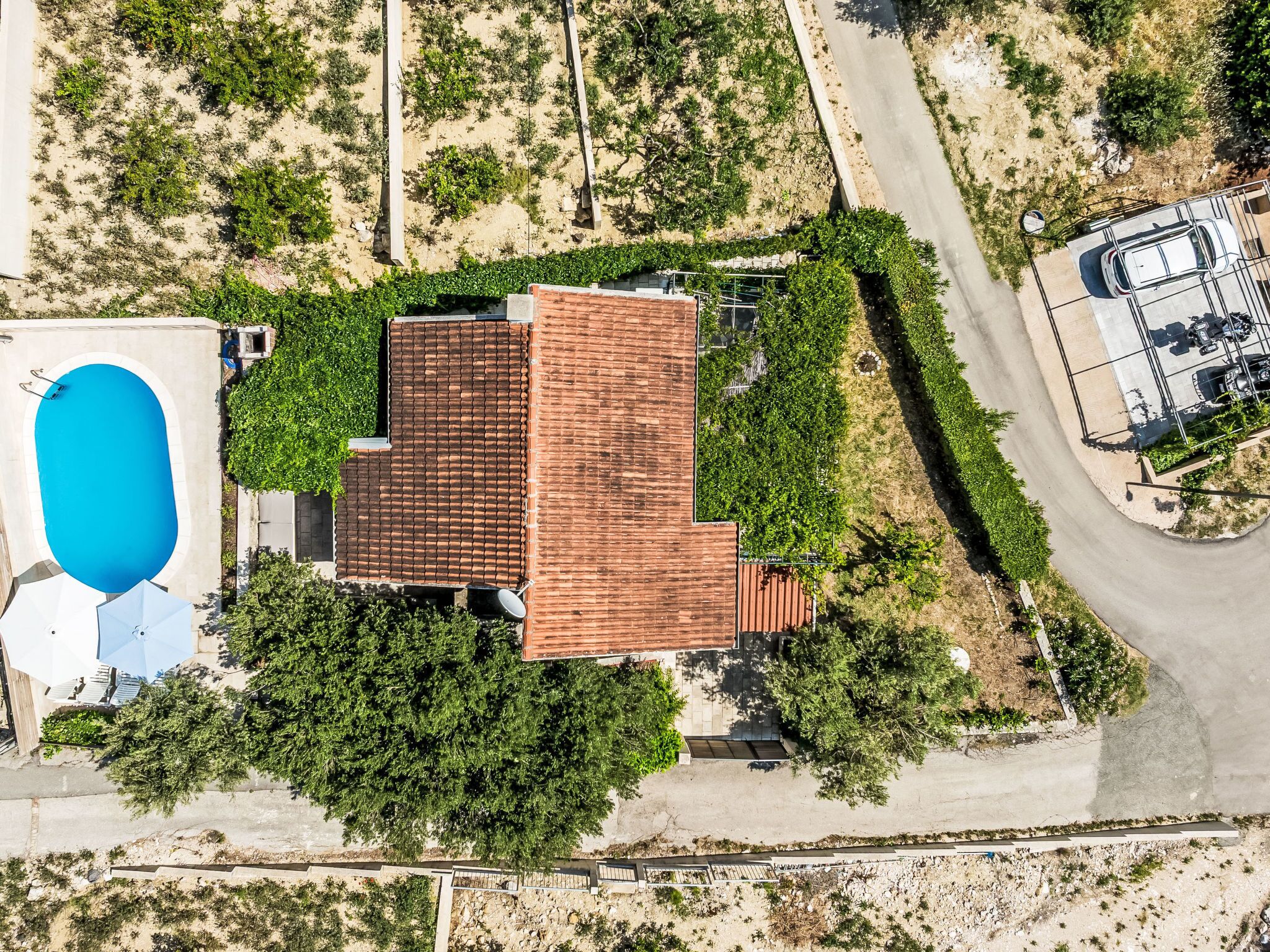 An aerial view of a property with a swimming pool, a fenced parking area, and a building with a tiled roof.