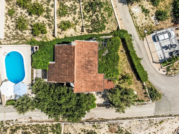 An aerial view of a property with a swimming pool, a fenced parking area, and a building with a tiled roof.