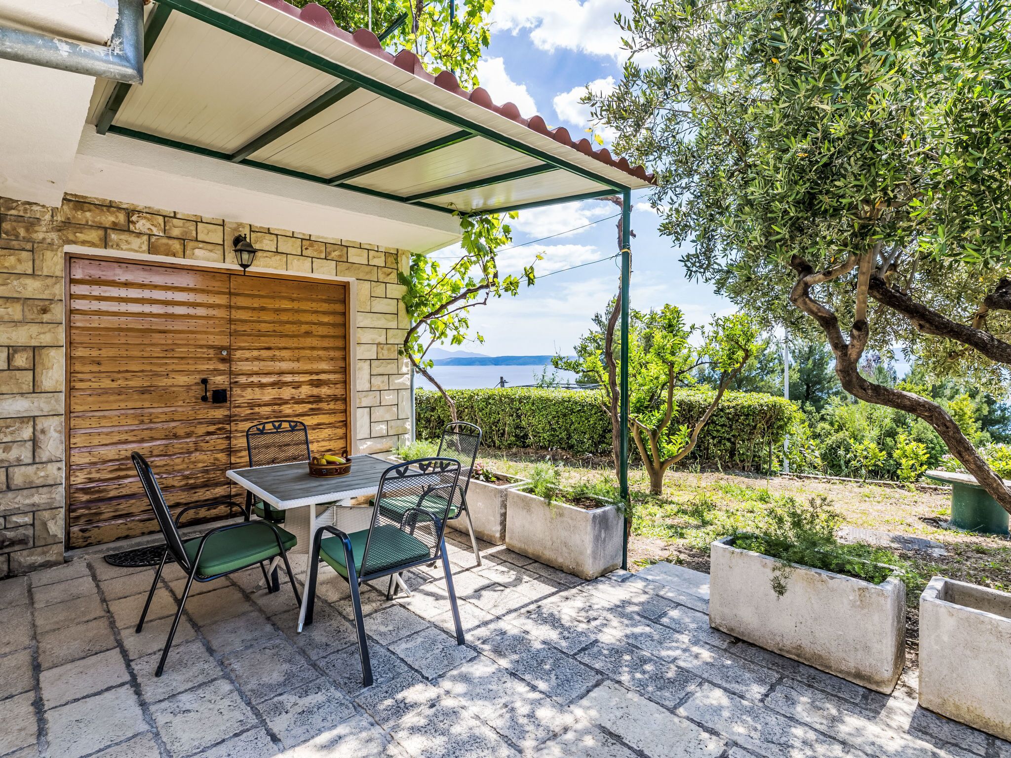 An outdoor patio with a table and chairs, a wooden door, and a view of the sea.