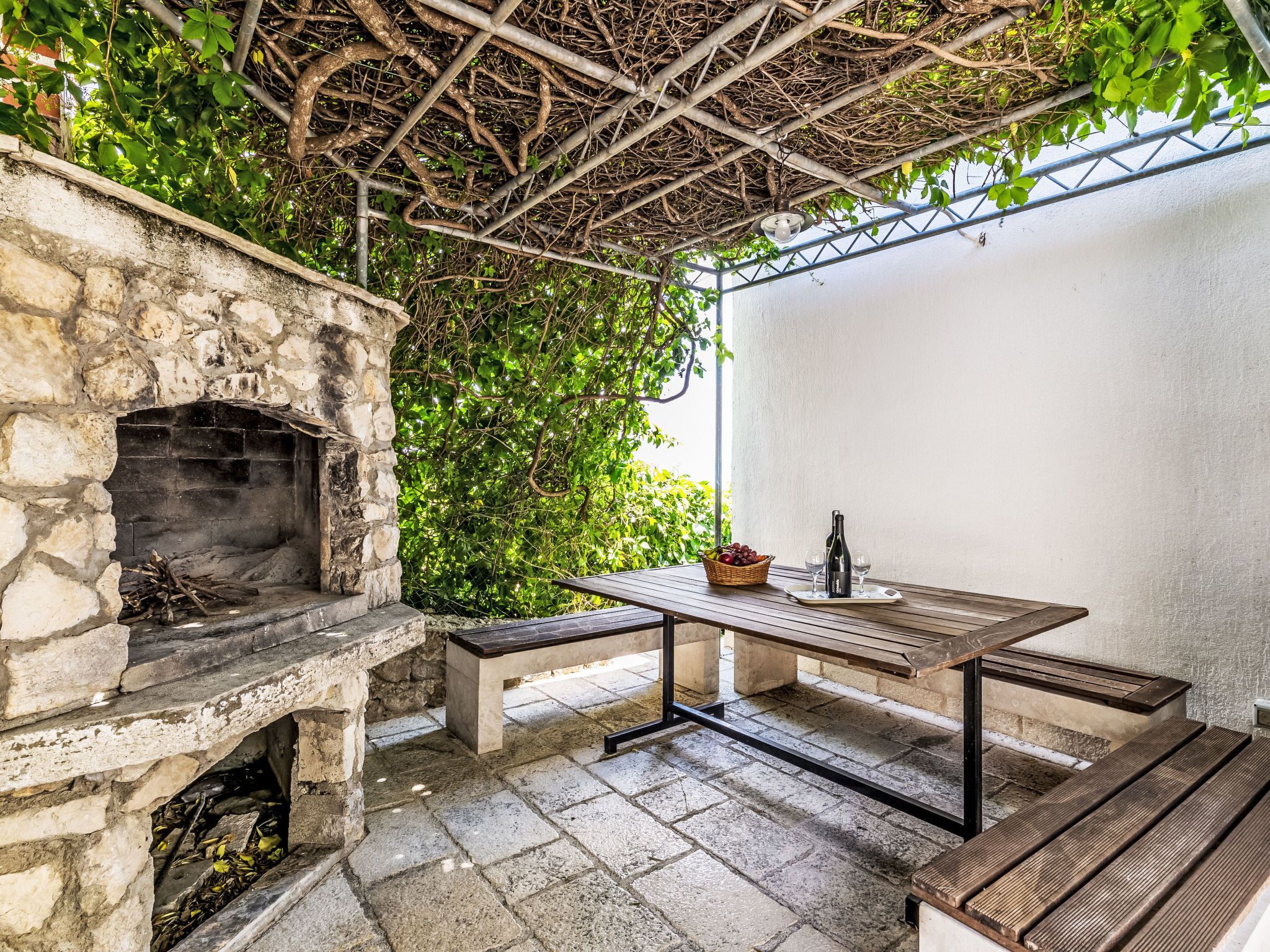 An outdoor patio with a stone fireplace, a wooden table, and benches.