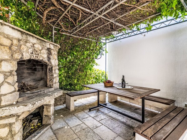 An outdoor patio with a stone fireplace, a wooden table, and benches.