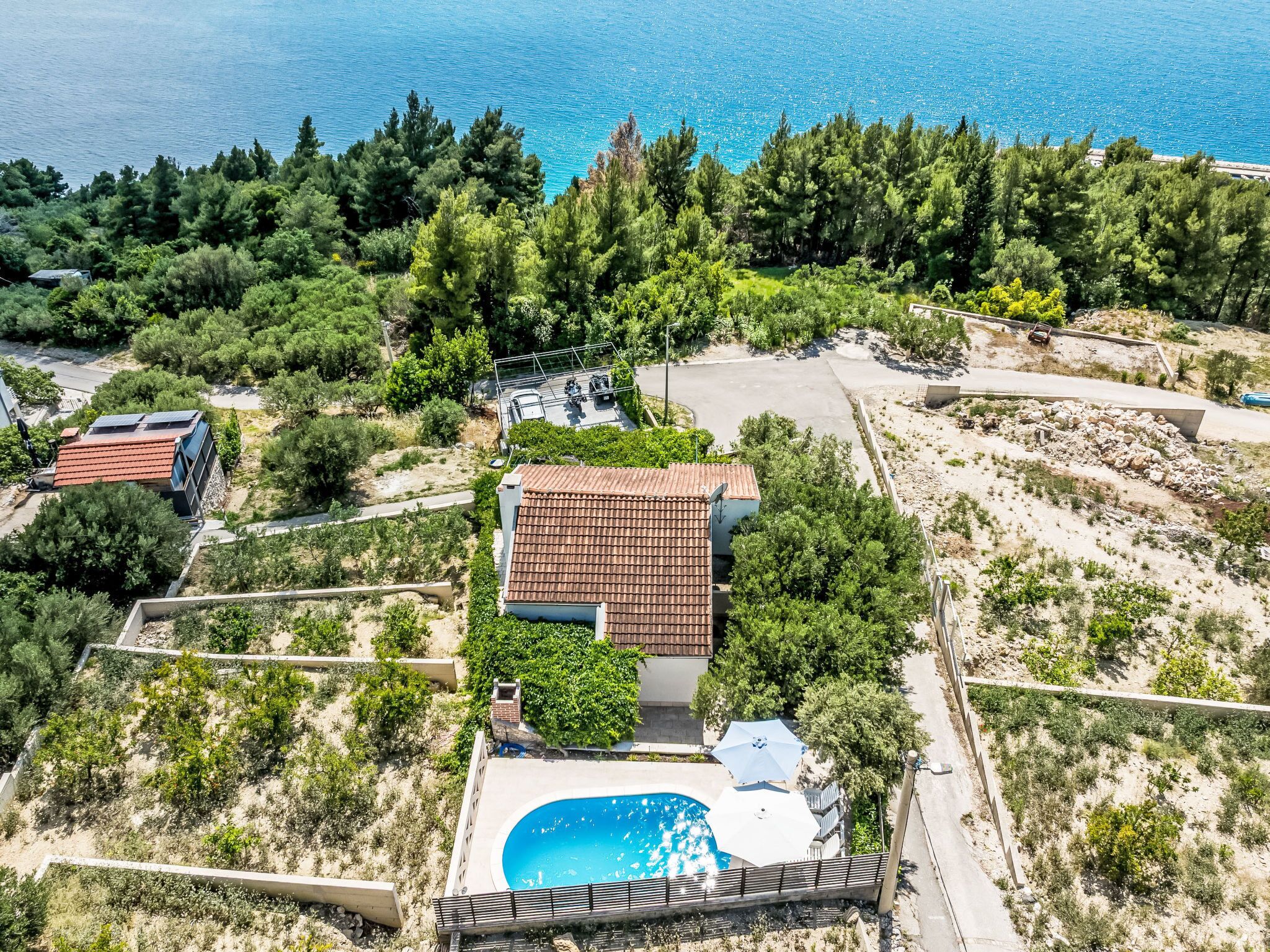 A residential area with a house featuring a swimming pool, surrounded by greenery and a clear view of the sea.