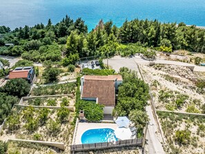 A residential area with a house featuring a swimming pool, surrounded by greenery and a clear view of the sea.