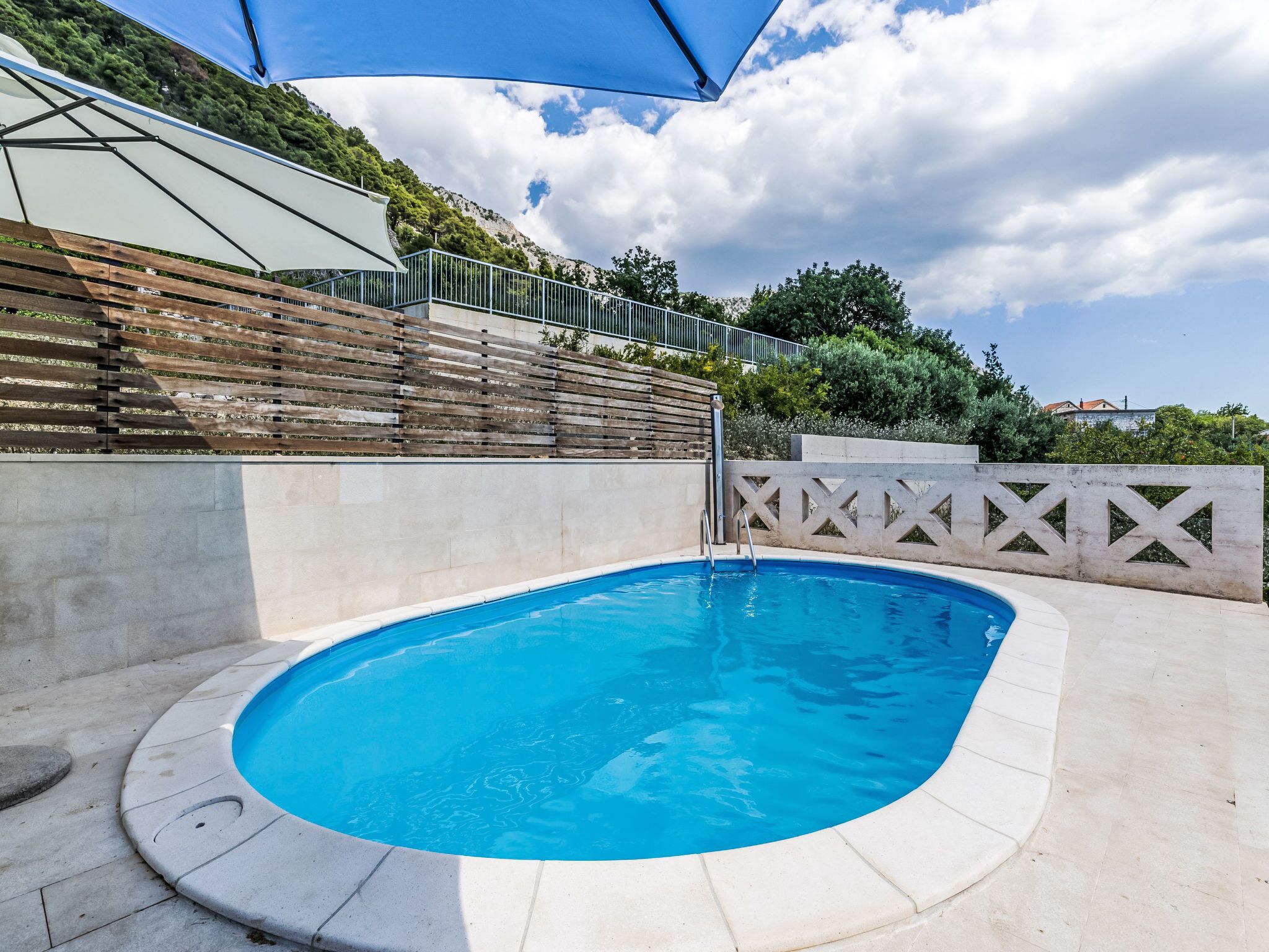 A swimming pool with a wooden deck, a concrete wall, and a metal fence.