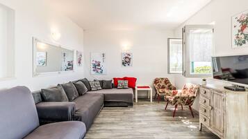 Ein modernes Wohnzimmer mit einem grauen Ecksofa, einem roten Sessel, einer Holzkommode und einem Fernseher.