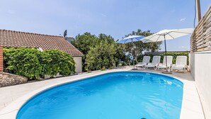 Una piscina amb terrassa enrajolada, envoltada de gandules i ombrelles, sota un cel serè.
