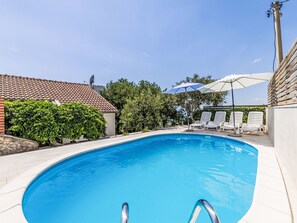 Een zwembad met betegeld zonnedek, omringd door ligbedden en parasols, onder een heldere lucht.