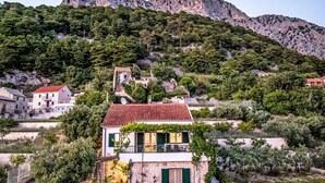 Una propietat a la vella amb una casa de pedra, teulada vermella, un balcó i vegetació abundant.