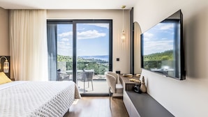 Habitación de hotel con cama, escritorio, silla, televisor y balcón con vistas.