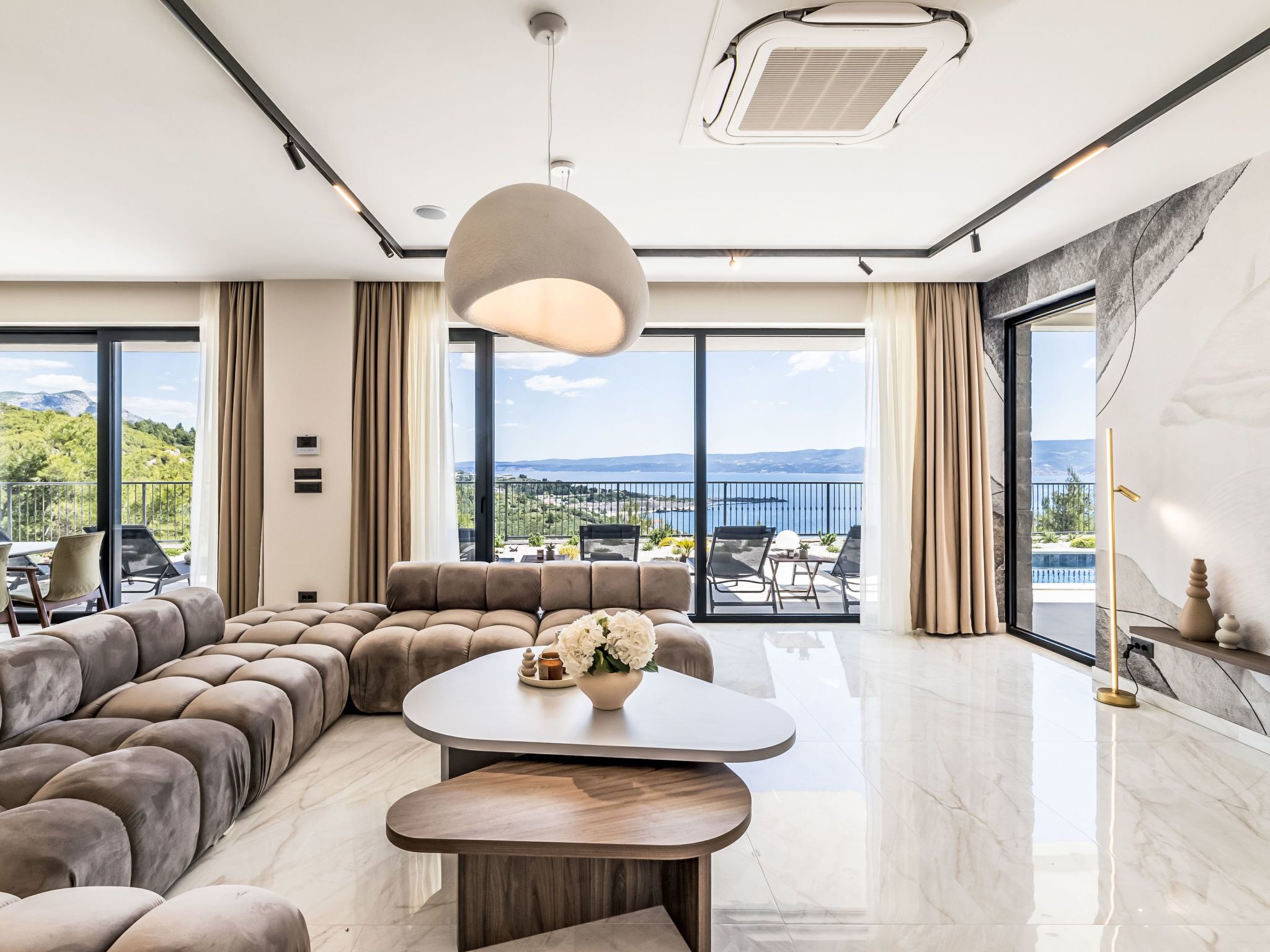 A spacious living room with a large sectional sofa, a round coffee table, and a view of a balcony with outdoor furniture.