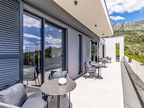 A modern outdoor patio with seating and tables, large windows, and a view of a mountainous landscape. - Vacation home M&D by Interhome (Dugi Rat)
