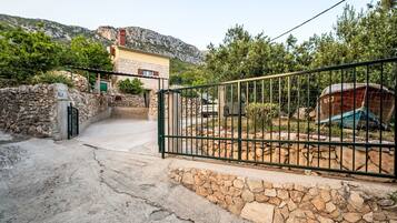 A stone wall entrance with a metal gate, a vehicle, and a building with a stone facade in the background.