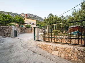 Entrada de pared de pedra amb una reixa de metall, un vehicle i un edifici amb façana de pedra al fons.