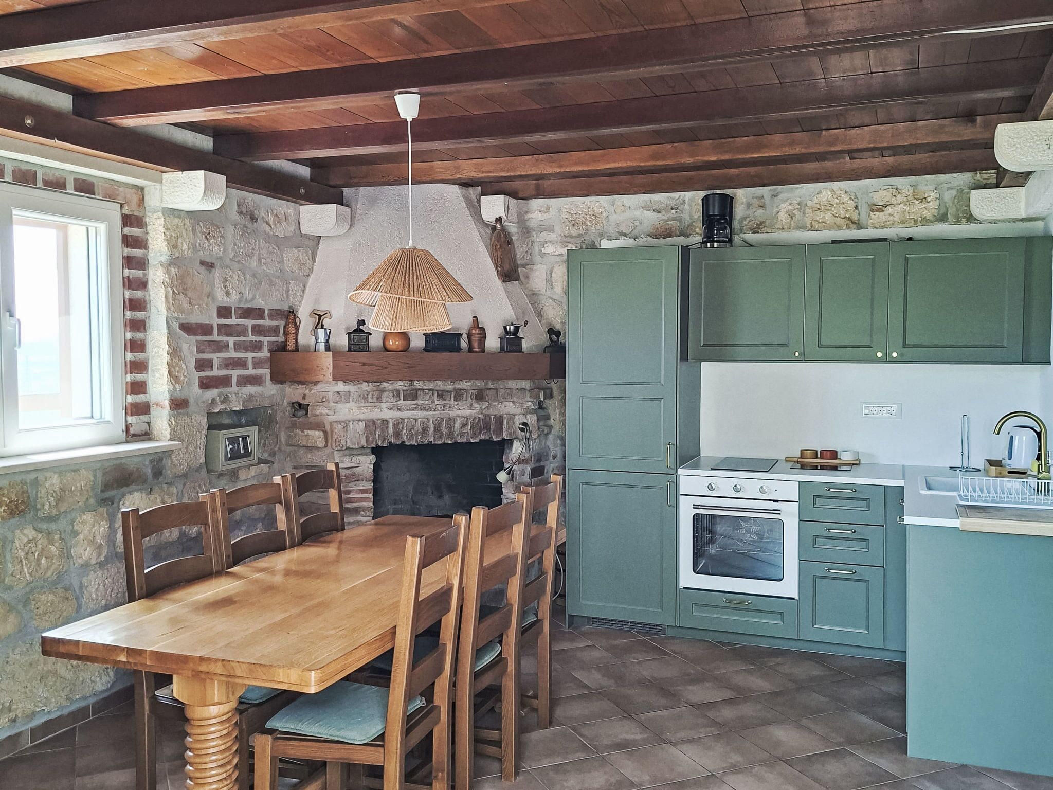 A rustic kitchen with a stone fireplace, wooden dining table, and teal cabinetry.