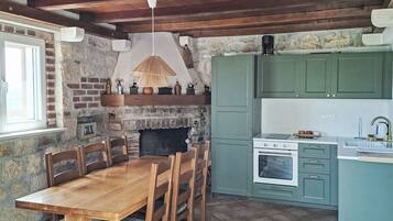 A rustic kitchen with a stone fireplace, wooden dining table, and teal cabinetry.