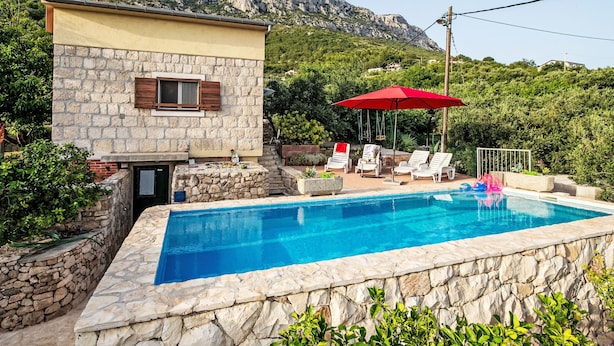 Un edificio de piedra con piscina, rodeado de vegetación y montañas al fondo.