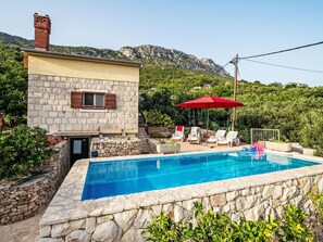 Edifici de pedra amb piscina, envoltat de vegetació i un paisatge de muntanya de fons.