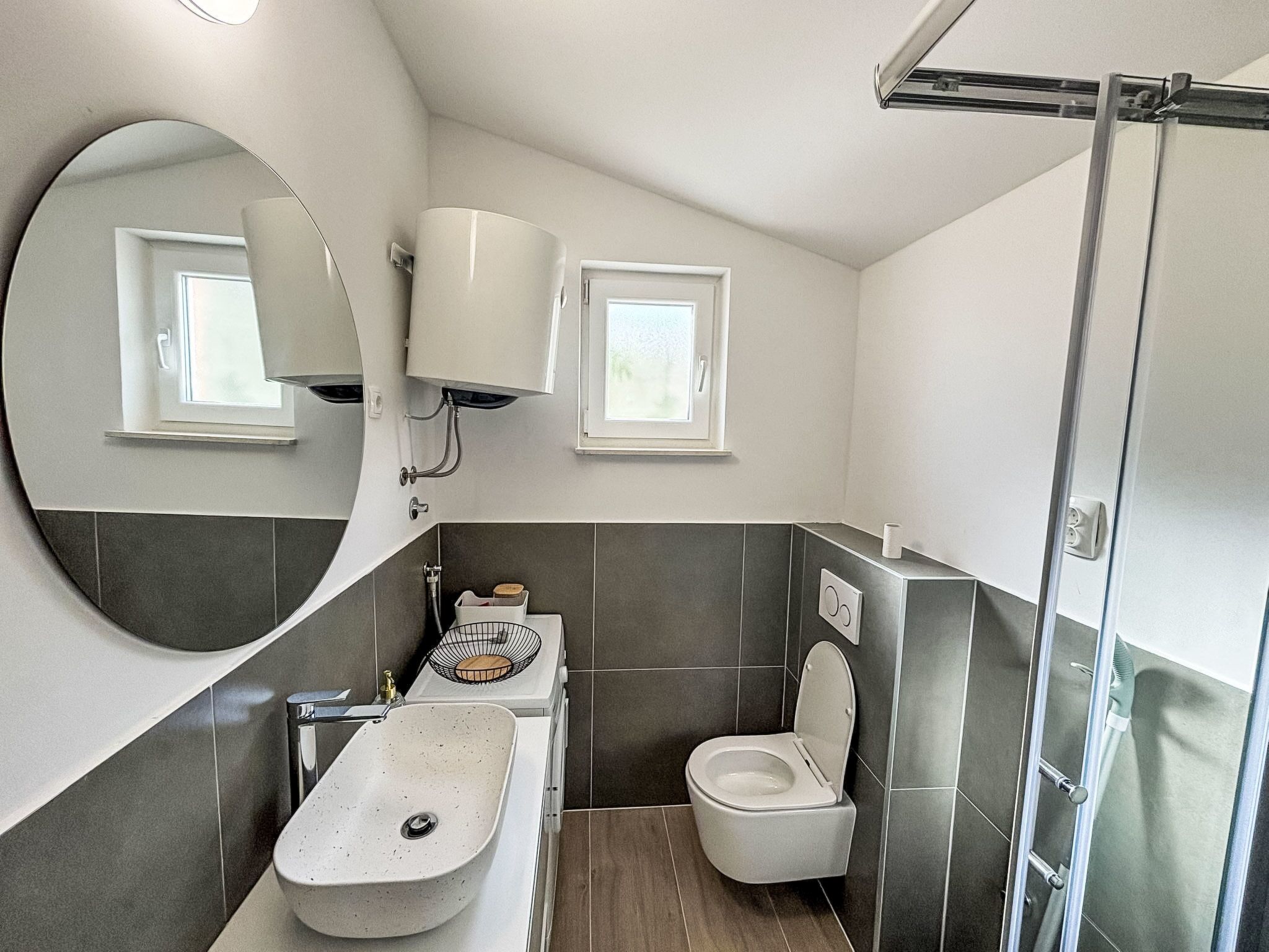 Un baño moderno con un espejo curvo, un lavamanos, un inodoro y una ducha.