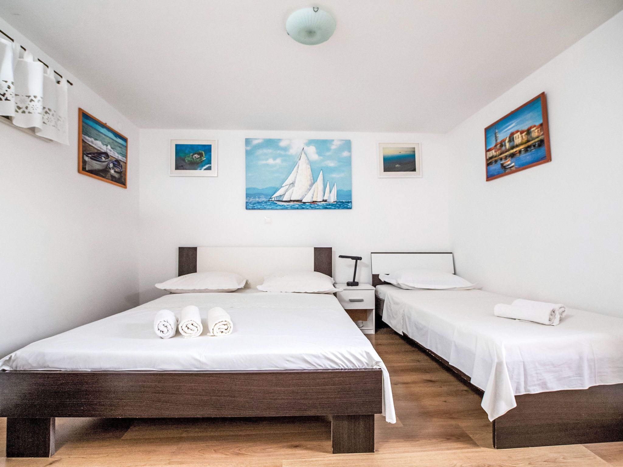 Ein Hotelzimmer mit einem großen Bett, zwei Einzelbetten, einem Nachttisch und einem Gemälde eines Segelboots an der Wand.