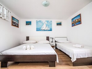 Habitación de hotel con una cama grande, dos camas más pequeñas, una mesita de noche y un cuadro de un velero en la pared.