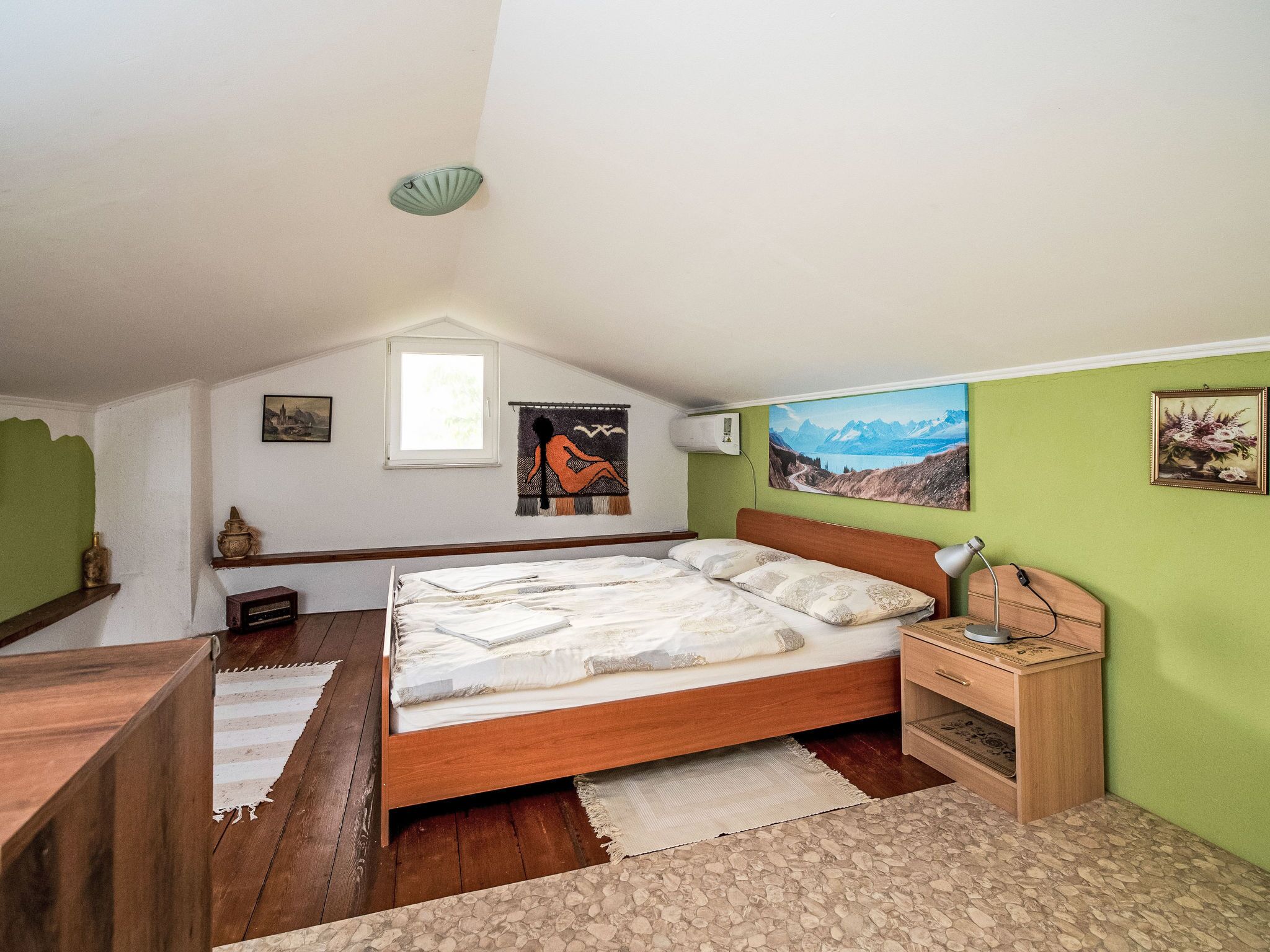A bedroom with a sloped ceiling, a bed, a nightstand, a desk, and artwork on the walls.
