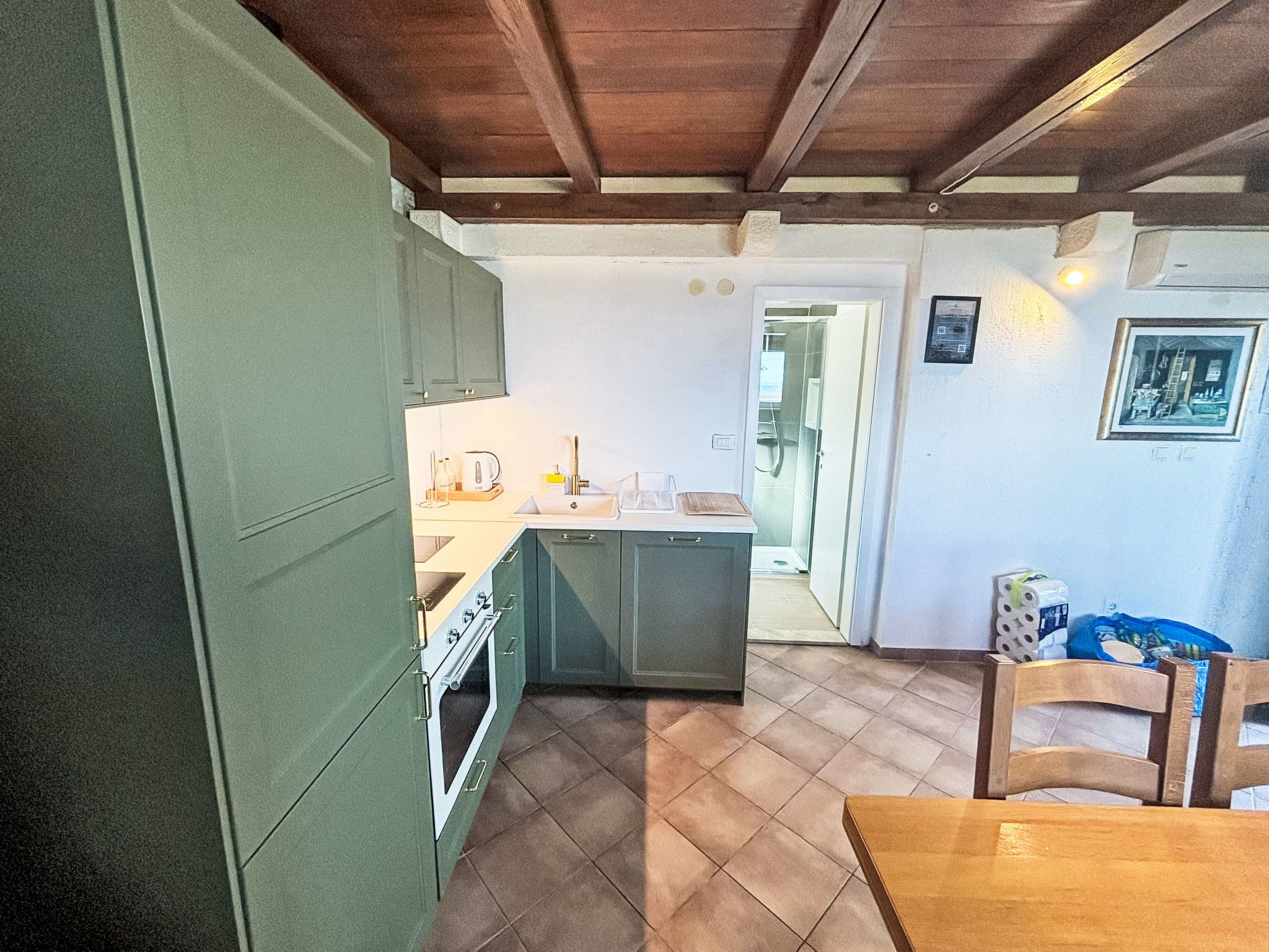 Une cuisine compacte dotée d’un four encastré, d’un petit îlot central avec un évier et d’un coin repas comprenant une table et des chaises en bois.