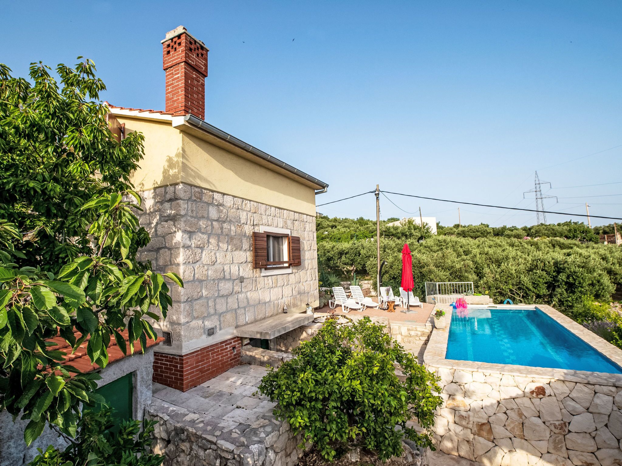 A two-story house with a stone facade, a swimming pool, and a garden with lounge chairs.