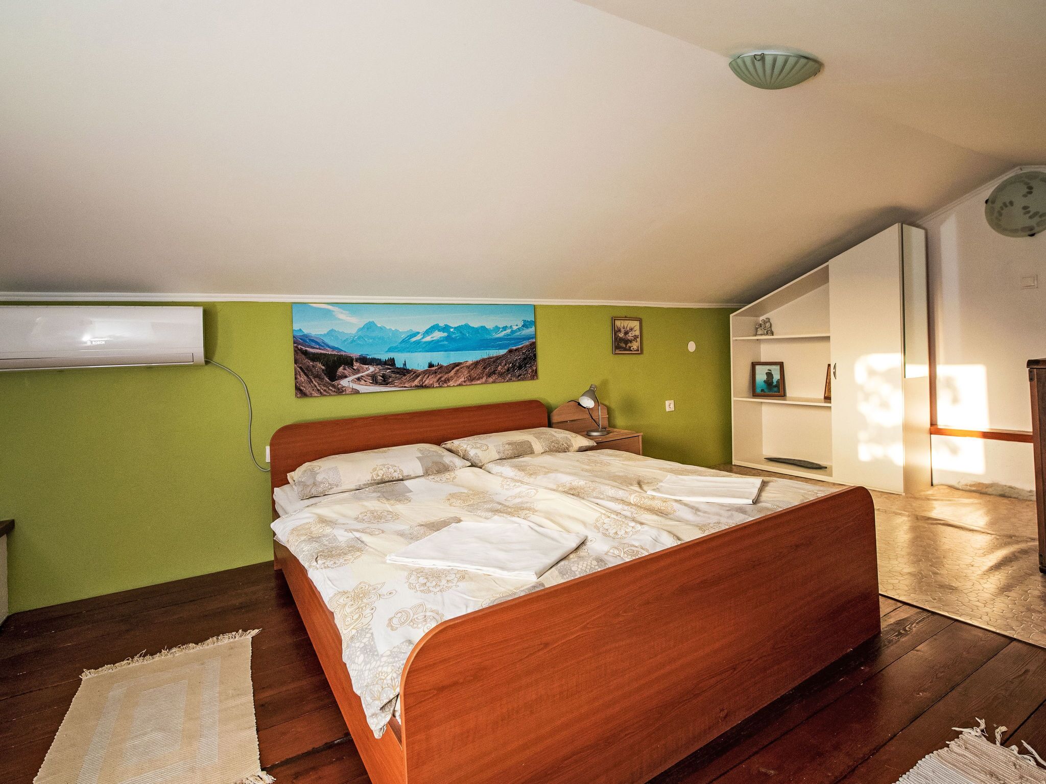 Une chambre avec un lit en bois, un mur vert, un tableau et une armoire blanche.