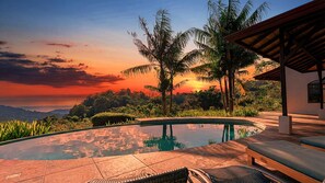 Ein Pool mit Blick auf einen Sonnenuntergang, umgeben von Palmen und einem Gebäude mit Dach.