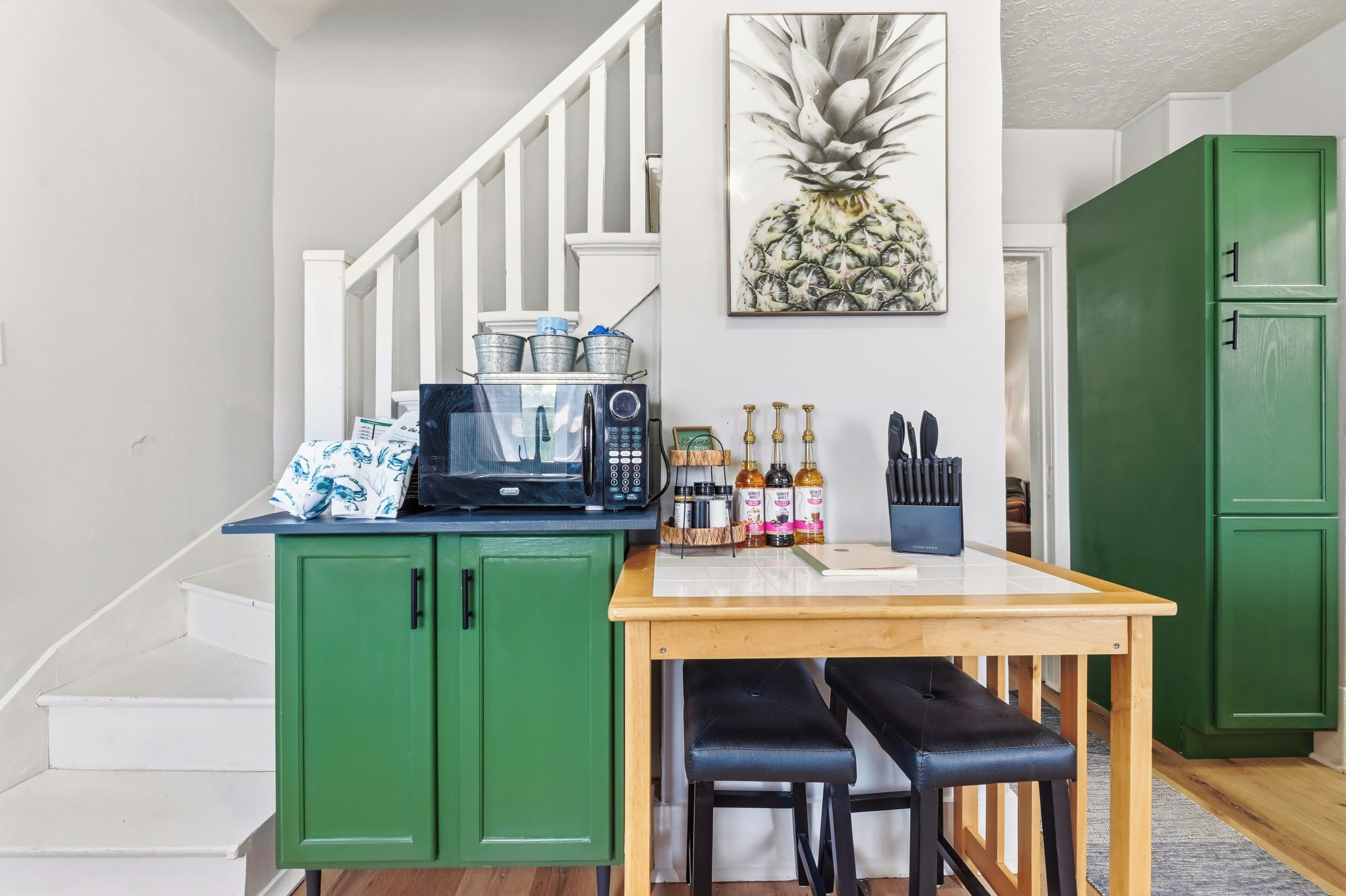 A kitchen with a microwave, green cabinets, a wooden table, and a chair.