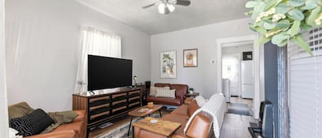 A living room with a flat-screen TV, leather sofas, a coffee table, and a ceiling fan.