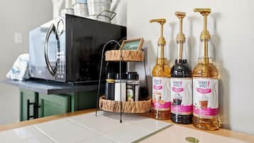Un comptoir de cuisine avec un four à micro-ondes, un étagère à épices à deux niveaux et trois bouteilles de sirop.