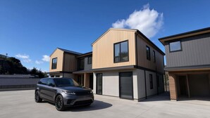 A modern two-story residential building with a car parked in front. - Lakehouse 62 – Brand New Lakefront Villa with Spa (Queenstown)