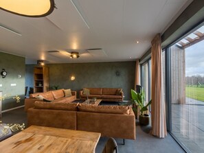 Ein modernes Wohnzimmer mit einem Ecksofa, einem Holztisch und einem großen Fenster mit Vorhängen.