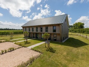 Un bâtiment moderne à deux étages, doté d’un toit en pente, entouré d’une pelouse bien entretenue et avec un vignoble en arrière-plan.