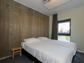 Ein Schlafzimmer mit einem Einzelbett, Holzwandverkleidung, einer kleinen Bank und einem Fenster mit Blick.