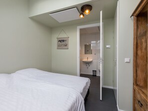 A bedroom with a bed, a hanging artwork, a ceiling light, and a view into a bathroom. - Zeebloesem by Interhome (Vrouwenpolder)