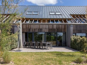 Un edificio moderno con tetto spiovente, ampie finestre e un’area salotto esterna.