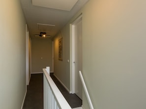 Ein schmaler Flur mit weißer Handlauf, Deckenventilator und einer Tür am Ende.