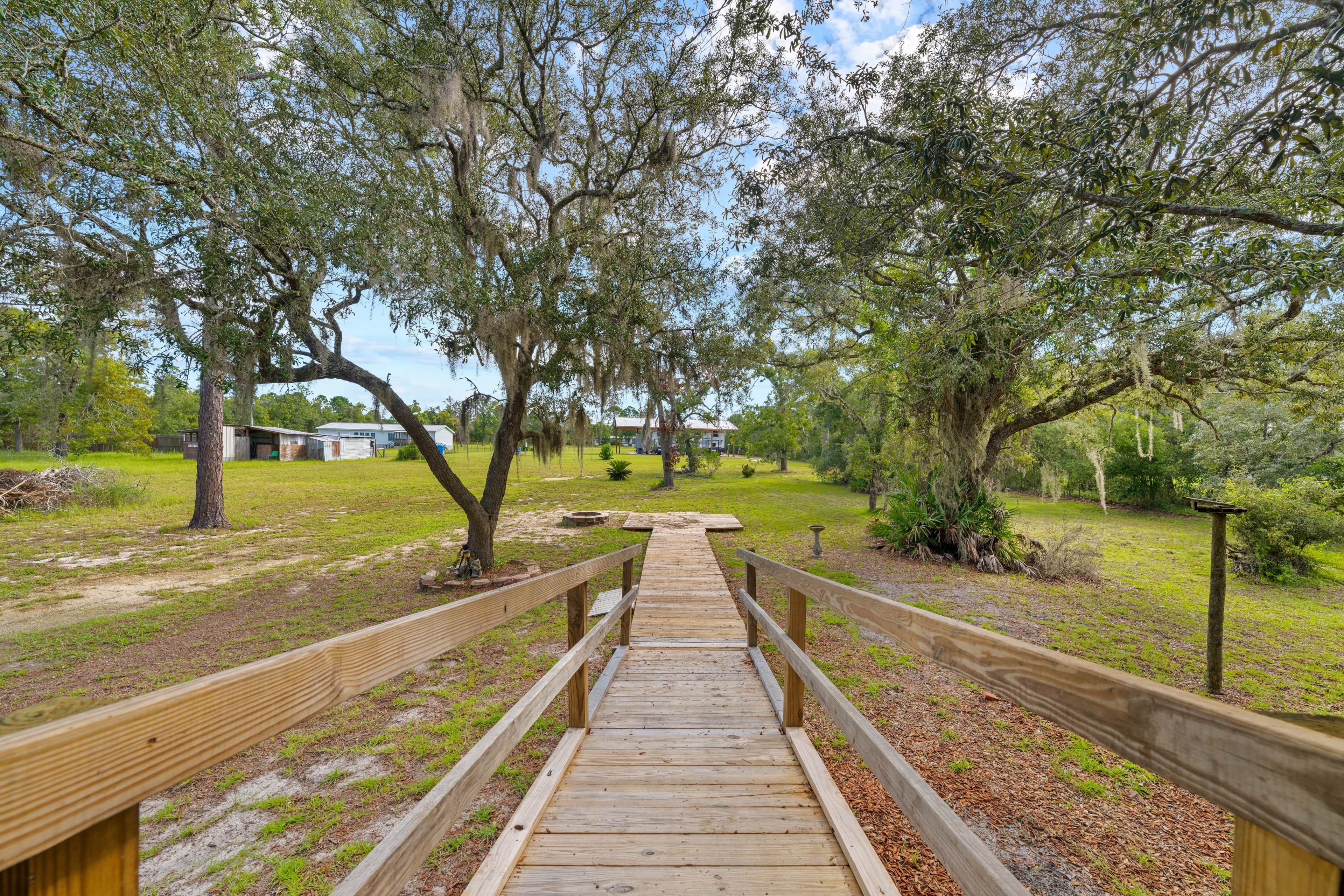 A wooden boardwalk leading through a park with trees and a building in the background.